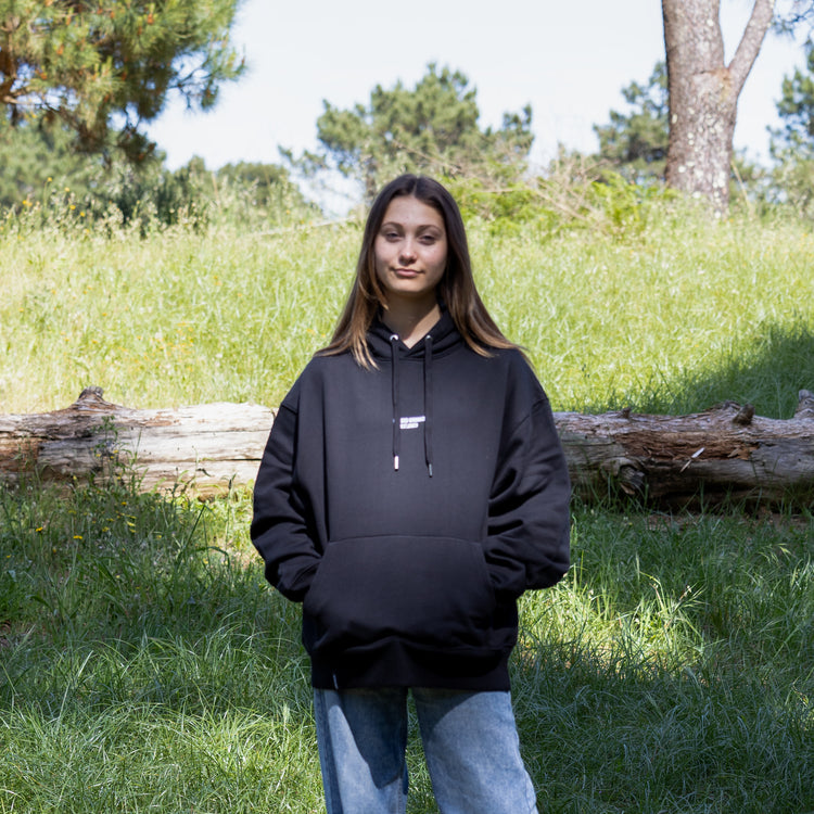 Kvindelig model i sort hoodie set forfra med hætten nede – 100% økologisk bomuld og moderne dansk design